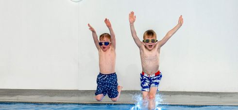 Two small boys jumping into a blue pool