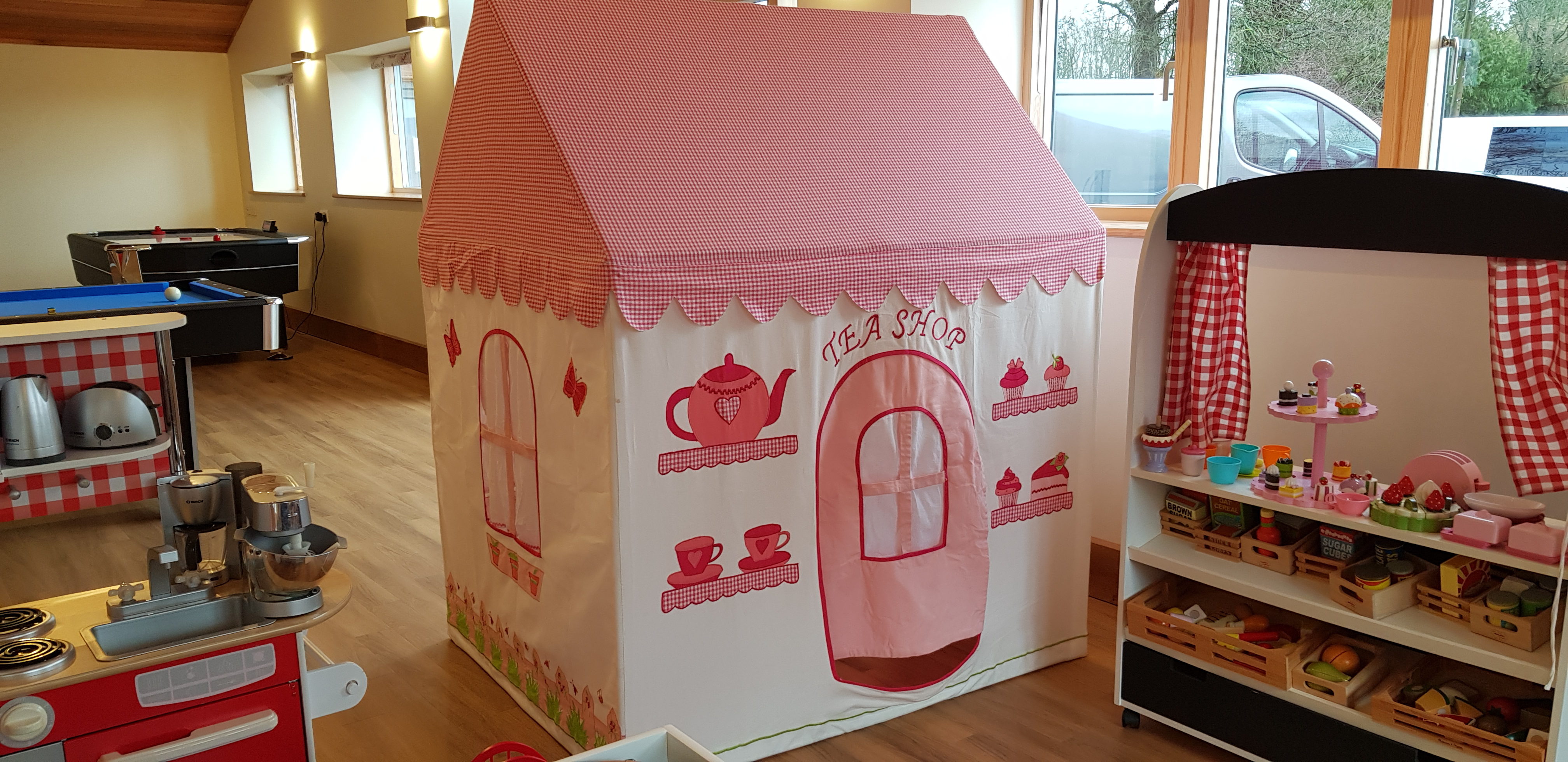 Showing a wendy house in pink and cream in a play room, wooden floors pretty curtains and door