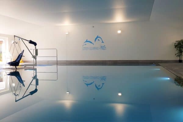 Blue swimming pool with accessible hoist and dolphin design on back wall