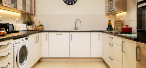 Hedgehunter kitchen with white and mock wooden units, large black clock on the wall, washer/dryer and dishwasher